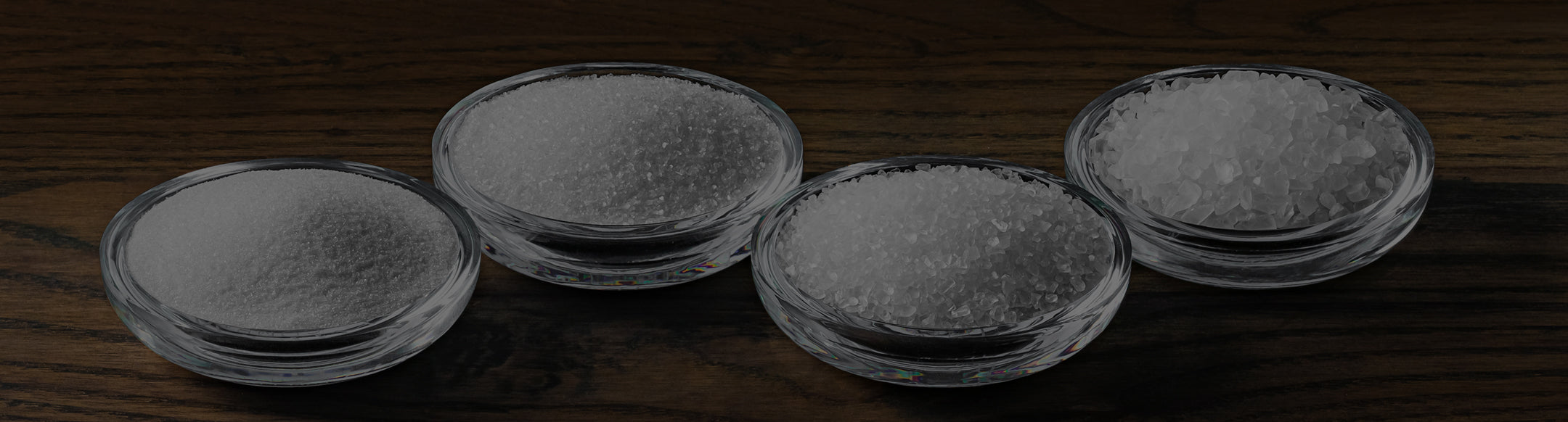 Four small glass bowls filled with salt on a wooden surface.